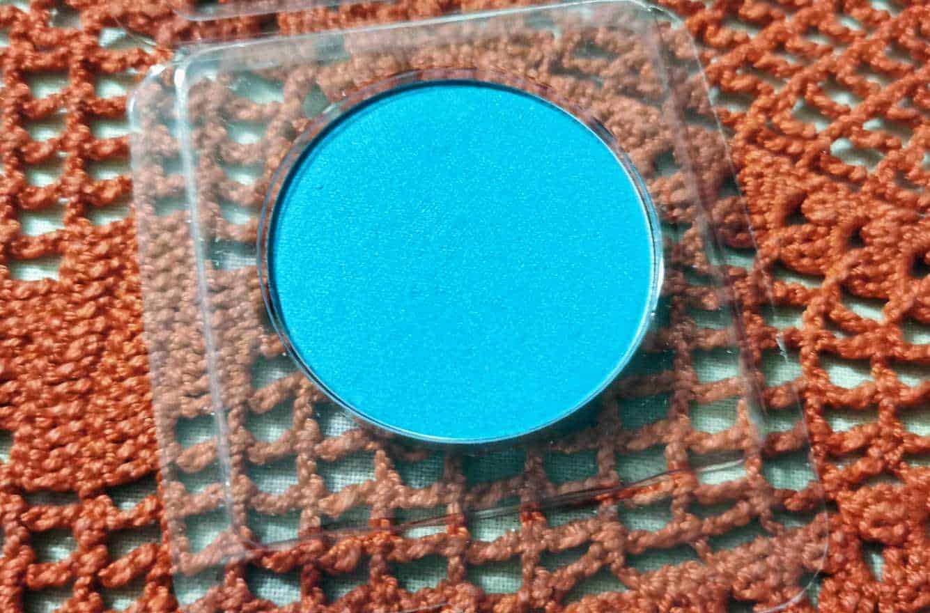 Blue eyeshadow in a round container on a textured orange background.