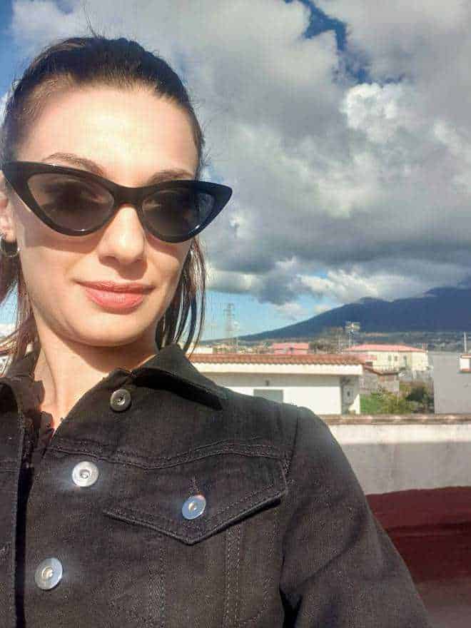 Sophisticated woman with sunglasses taking selfie outdoors on a bright day in Italy.