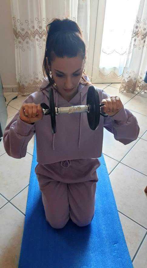 Scolara adolescente che fa esercizi di fitness con manubri su tappetino yoga in casa.
