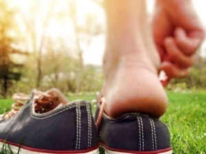 Scarpa da ginnastica posizionata sull'erba con una persona che si lega la scarpa, ambientazione all'aperto con luce naturale, stile casual, perfetta per articoli su sport.