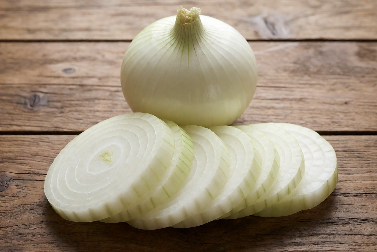 Cipolla bianca fresca intera e affettata su tavolo in legno per cucina, alimento naturale e salutare.
