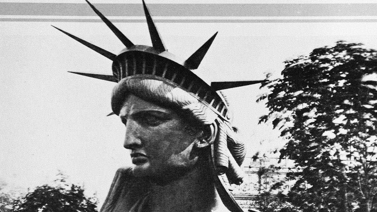 Statua della Libertà in stile vintage, foto in bianco e nero, simbolo di libertà e democrazia, raffigurante una donna con diadema a raggi. Scena urbana con alberi sullo sfondo, atmosfera retrò.