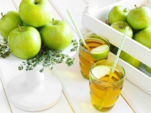 Mele verdi e bicchieri di sidro di mele fresco con cannucce su sfondo chiaro, presentazione di bevande naturali a base di mela, ideale per blog di ricette healthy e lifestyle.