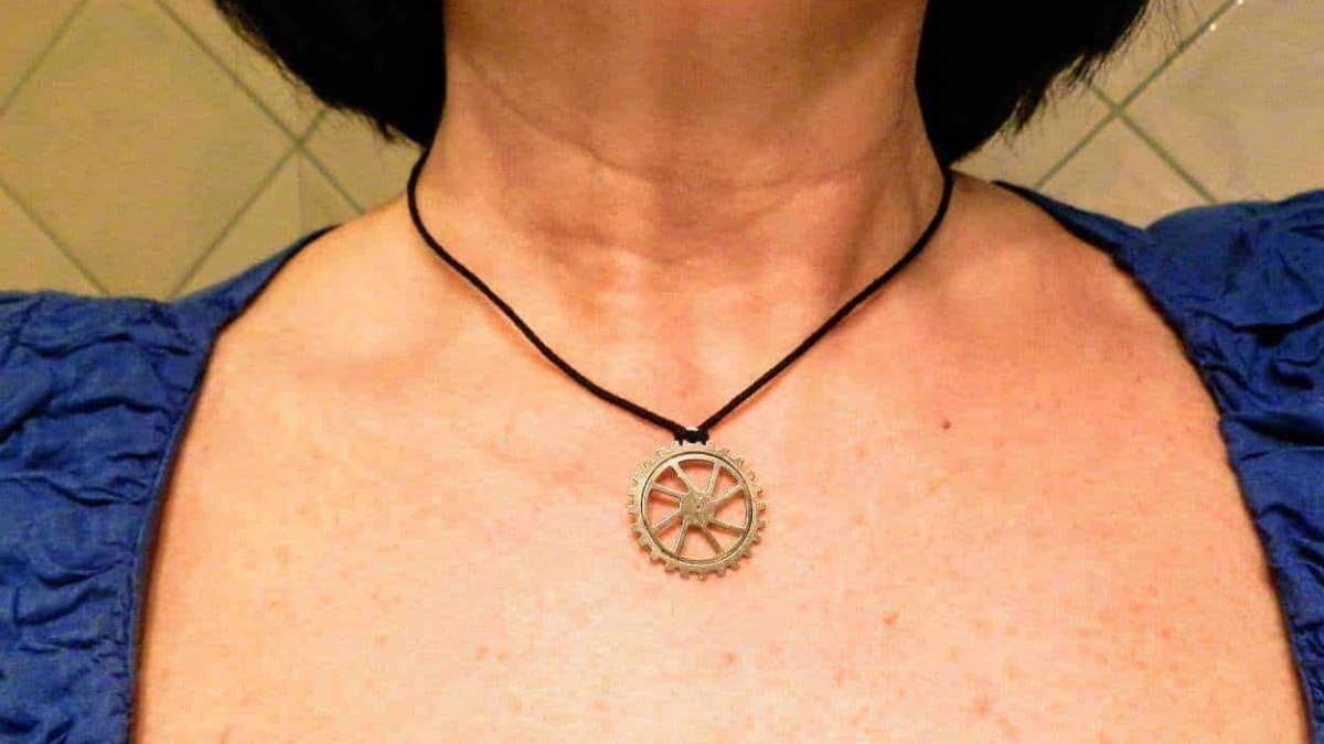 Fornitura di un collier con ciondolo a ingranaggio su una persona, foto di dettaglio del collo e parte superiore del petto, con sfondo di piastrelle beige.