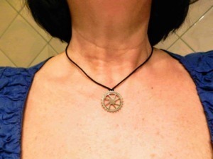 Fornitura di un collier con ciondolo a ingranaggio su una persona, foto di dettaglio del collo e parte superiore del petto, con sfondo di piastrelle beige.