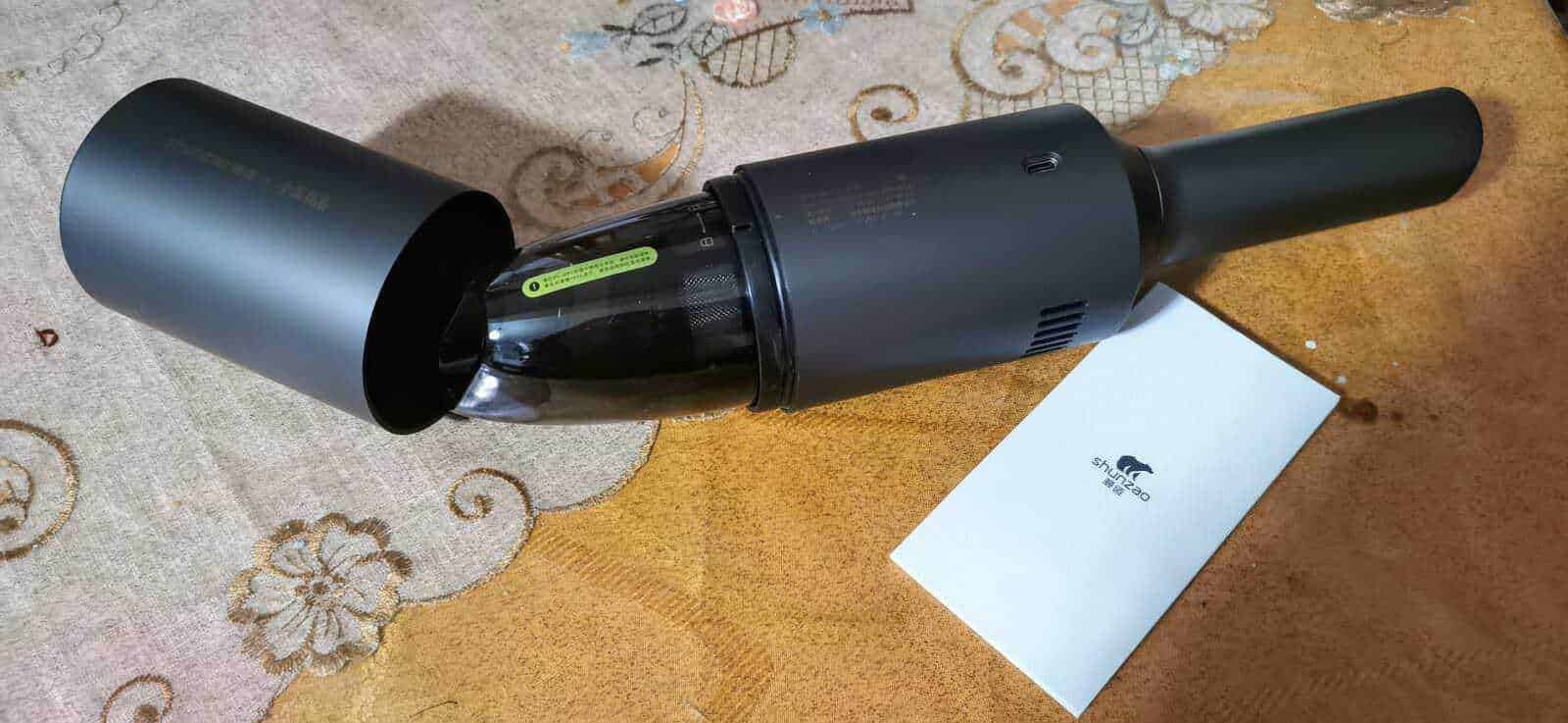 Aspirapolvere per auto senza fili XIAOMI SHUNZAO Mijia Z1 4 Aspirapolvere senza fili Dyson V15 Detect in colore nero, posizionato su un tavolo di legno chiaro con dettagli decorativi, perfetto per la pulizia moderna ed efficiente della casa.
