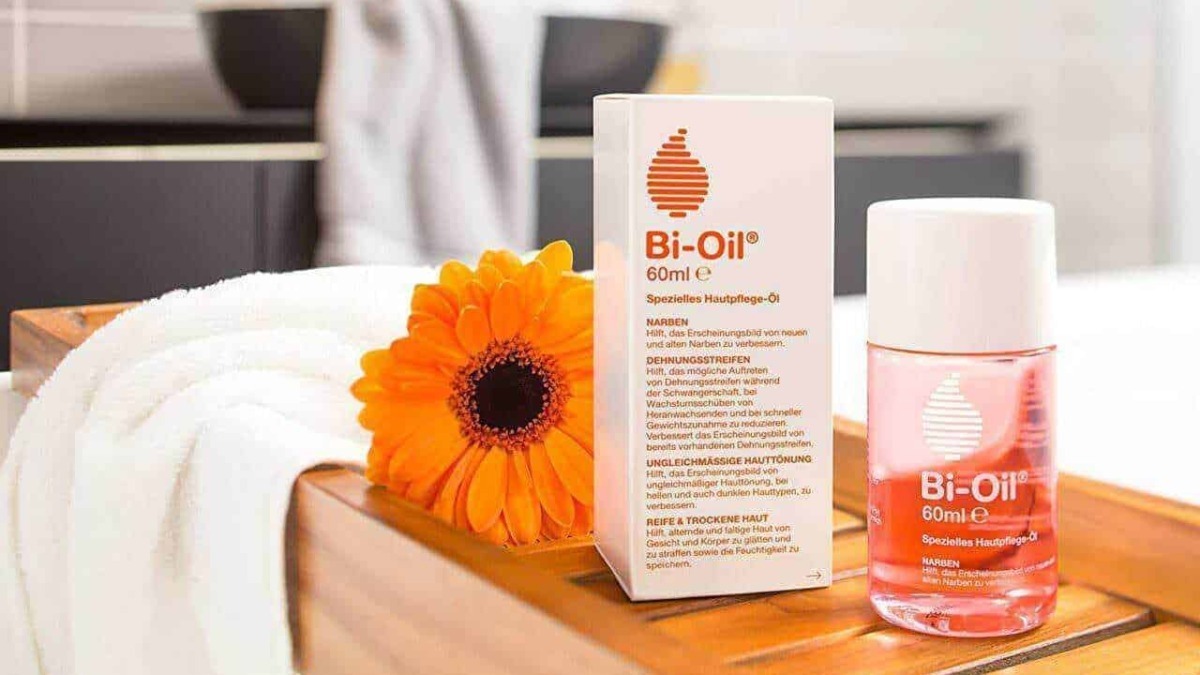 Olio Bi-Oil e unguento per il trattamento delle cicatrici e della pelle screpolata, posizionato su un tavolo di legno con una fiore arancione accanto.