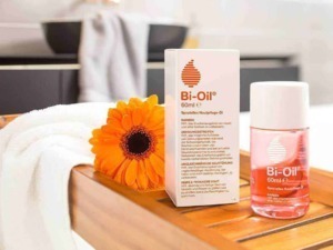 Olio Bi-Oil e unguento per il trattamento delle cicatrici e della pelle screpolata, posizionato su un tavolo di legno con una fiore arancione accanto.