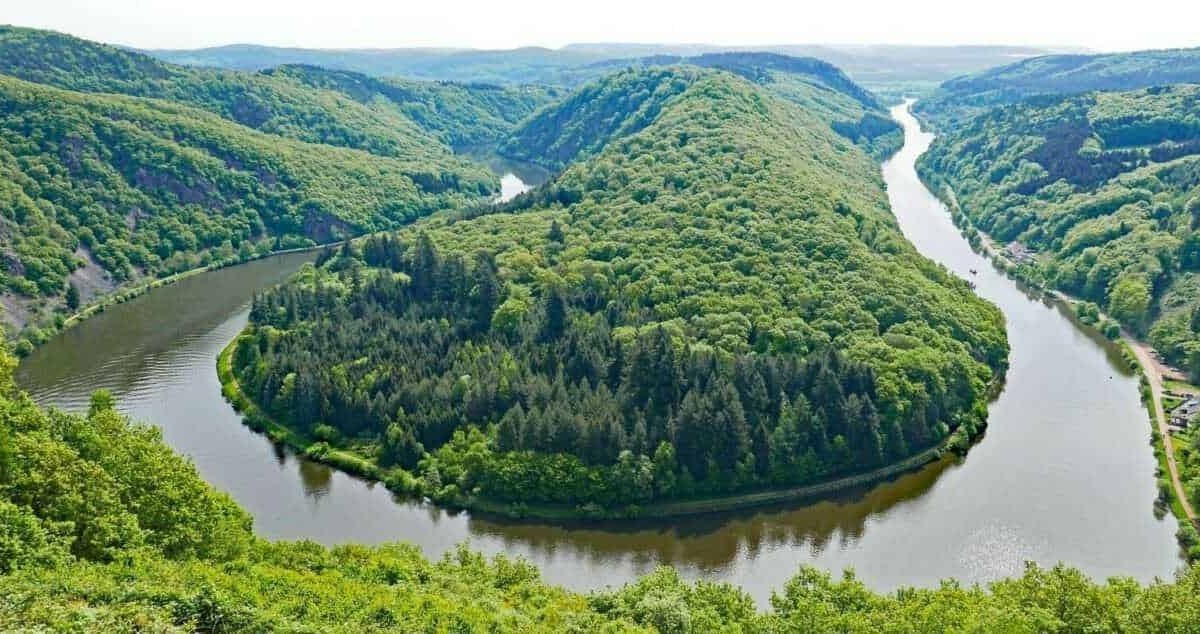 Lago in forma di cuore circondato da verdi colline e foreste, con un fiume che lo circonda completamente, in una pittoresca area naturale italiana.