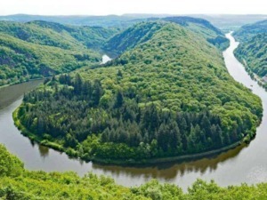 Lago in forma di cuore circondato da verdi colline e foreste, con un fiume che lo circonda completamente, in una pittoresca area naturale italiana.