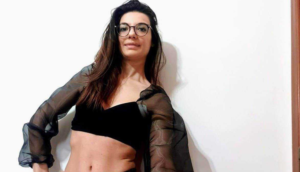 Elegante donna con occhiali e outfit trendy, posa con self-confidence contro parete bianca, ideale per immagini di stile di vita, moda e blog personale.