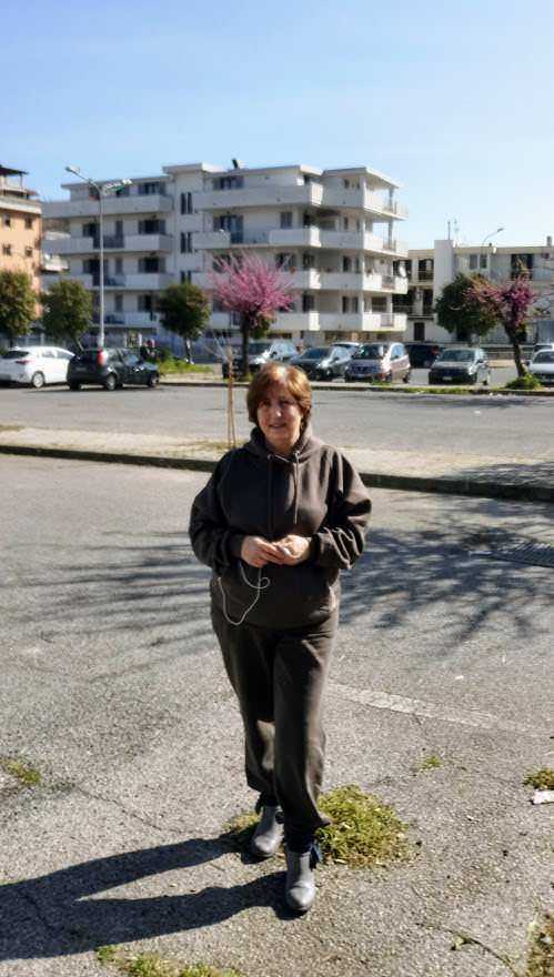 Appunti Sul Blog, donna che cammina nel quartiere urbano con edifici residenziali e alberi in fiore, scenario di vita quotidiana.
