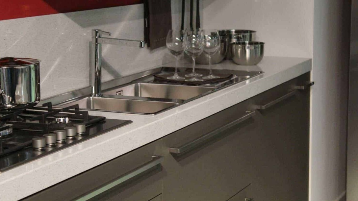 Davanti a lavello con piatti e bicchieri in cucina moderna, superficie in marmo, attrezzature in acciaio inox.