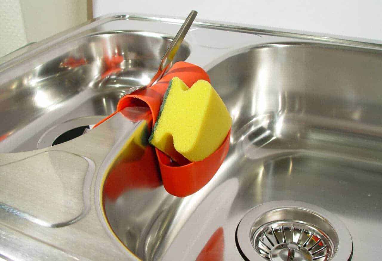 Panni da cucina attaccati a un lavello in acciaio inox con spugnetta gialla e detergente rosso.