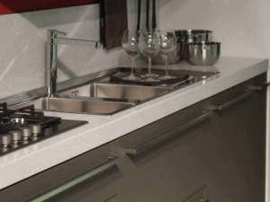 Davanti a lavello con piatti e bicchieri in cucina moderna, superficie in marmo, attrezzature in acciaio inox.
