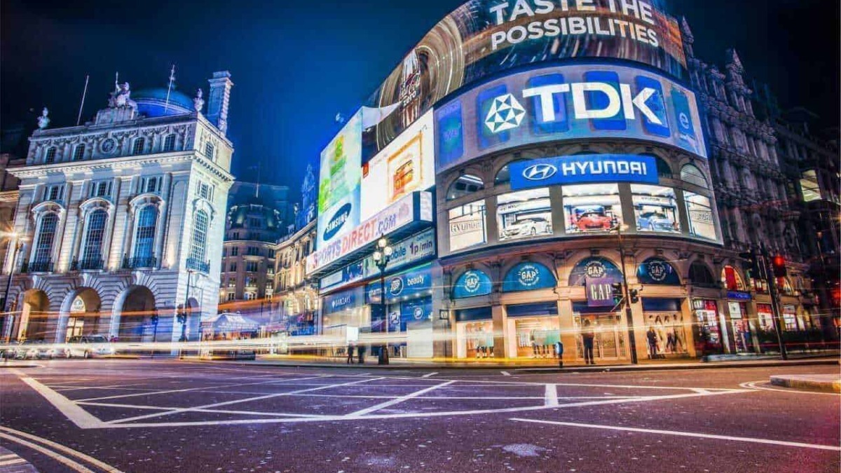 Città di Londra di notte con schermi pubblicitari digitali e traffico trafficato, promozioni di brand come Hyundai e TDK, atmosfera urbana vivace, pubblicità luminose e architettura storica.