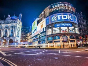 Città di Londra di notte con schermi pubblicitari digitali e traffico trafficato, promozioni di brand come Hyundai e TDK, atmosfera urbana vivace, pubblicità luminose e architettura storica.