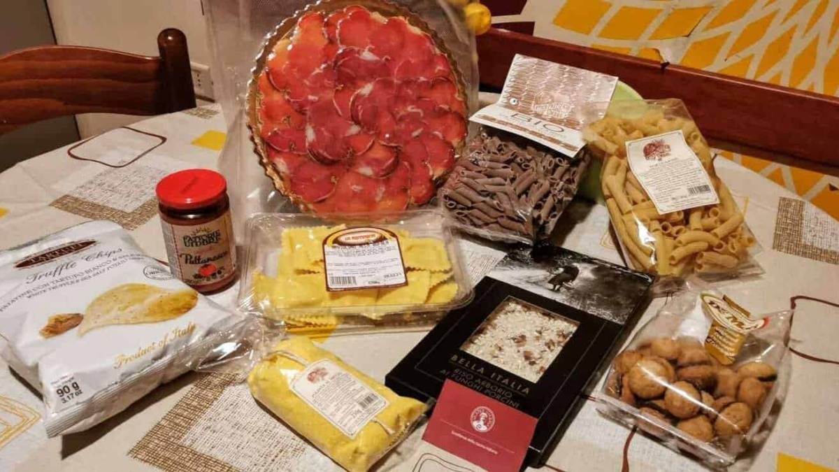 Freschissimo salumi e pasta italiana, formaggi, crackers e snack tipici, disposti su tovaglia a quadretti, pronti per un aperitivo o una cena autentica italiana.
