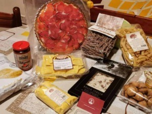 Freschissimo salumi e pasta italiana, formaggi, crackers e snack tipici, disposti su tovaglia a quadretti, pronti per un aperitivo o una cena autentica italiana.