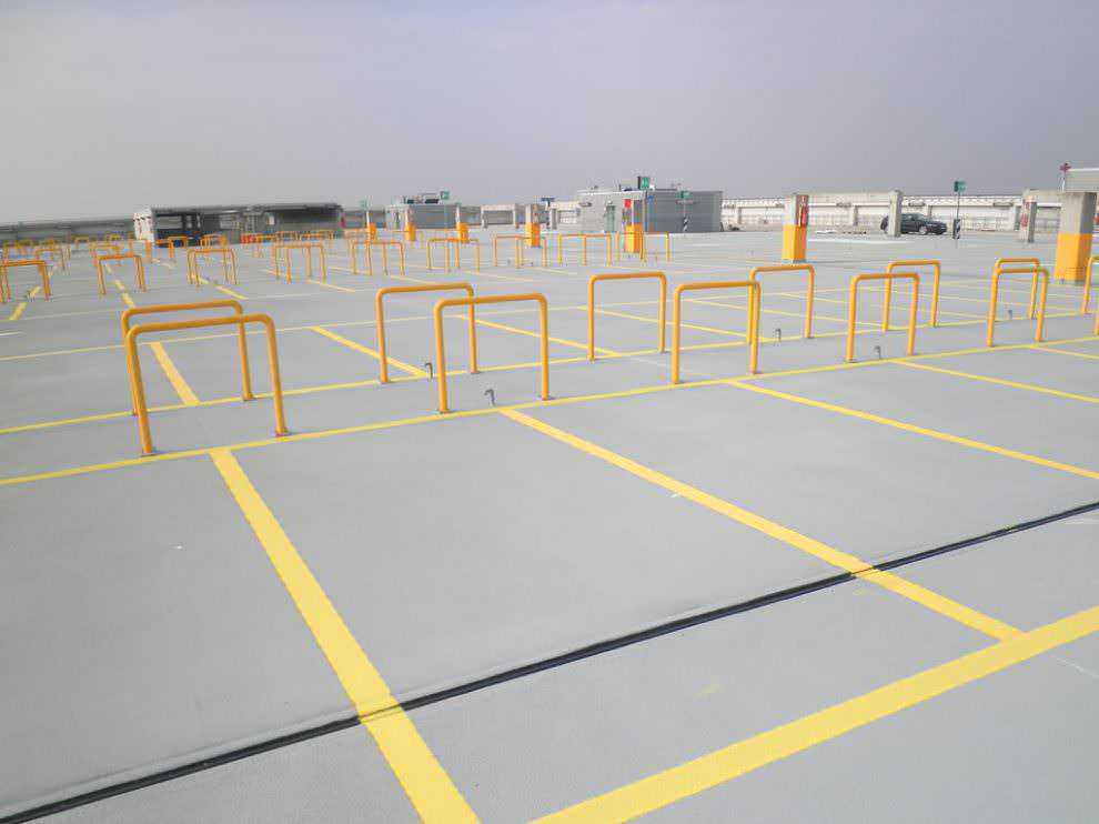 Poliurea, impermeabilizzazione a spruzzo dei parcheggi. Parcheggio per auto in un grande parcheggio coperto con barriere di sicurezza gialle, spazio per diverse vetture, senza veicoli in sosta, in un'area moderna e ben segnalata.