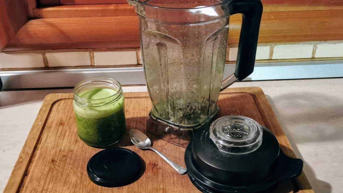 Frullatore con residui di verdura, barattolo di succo di cetriolo, e accessori su un tagliere di legno in cucina, ideali per preparare smoothies e detox.
