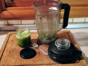 Frullatore con residui di verdura, barattolo di succo di cetriolo, e accessori su un tagliere di legno in cucina, ideali per preparare smoothies e detox.