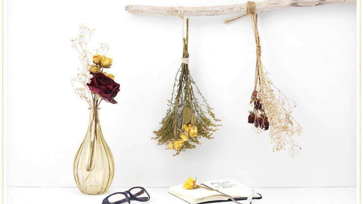Vaso con fiori secchi, appunti e occhiali, decorazioni floreali sospese, atmosfera minimalista e elegante.