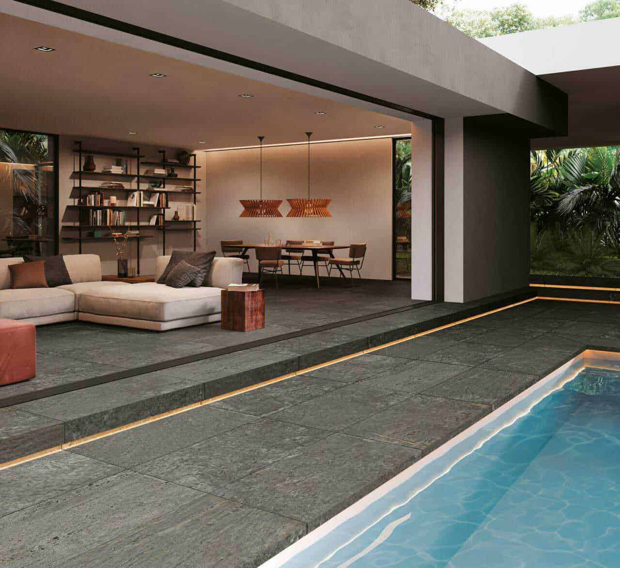 Ampia zona living con divano beige e libreria moderna, spazi esterni con piscina e giardino tropicale, arredamento elegante e design contemporaneo, ideale per case di lusso e relax docce in piscina.