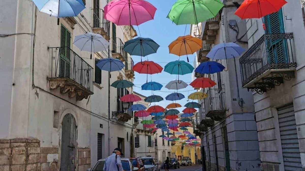 Colorati ombrelli appesi sopra strade di un quartiere storico, decorazione artistica e colorata creata per abbellire l'ambiente e attirare visitatori, perfetta per foto e giornate di sole.
