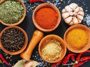 Miscela di spezie e aromi in ciotole di legno con aglio, pepe nero, curcuma, paprika e cumino, su sfondo nero.