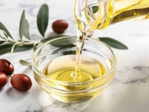 Olio extravergine di oliva puro in una ciotola di vetro, con foglie di ulivo e frutti di olivo su sfondo bianco, suggestione di cucina salutare e naturale.