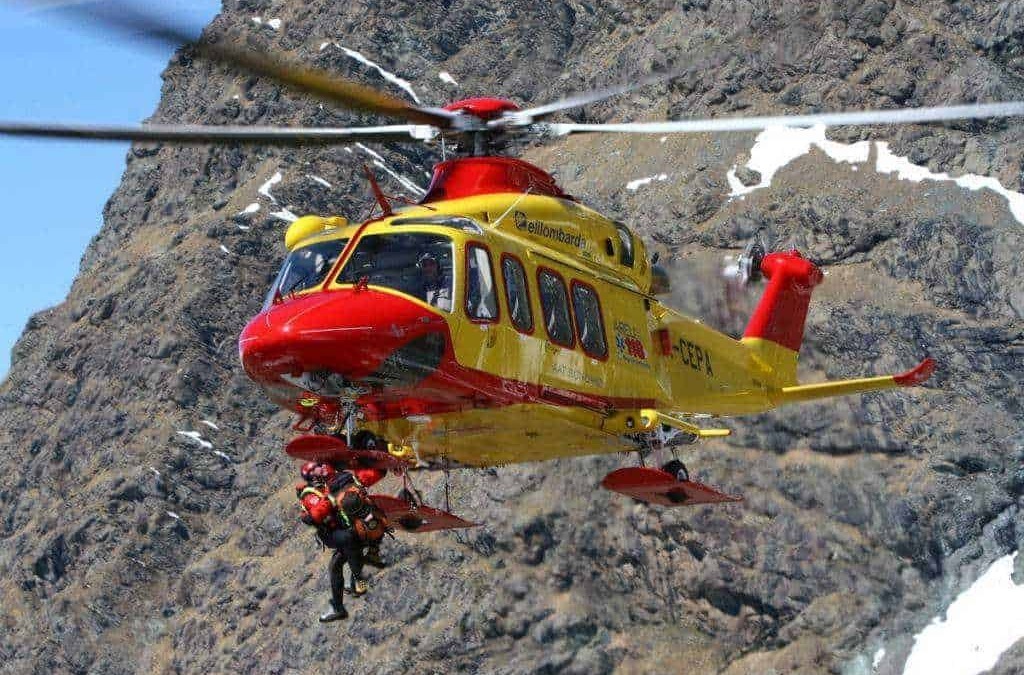 Elicottero di soccorso alpino in azione su pareti di roccia montana con operatori di emergenza in attività di salvataggio. Ricerca e intervento in ambienti montani difficili.