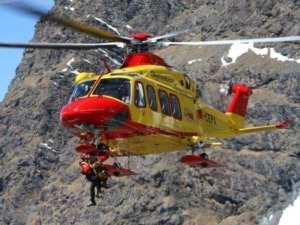 Elicottero di soccorso alpino in azione su pareti di roccia montana con operatori di emergenza in attività di salvataggio. Ricerca e intervento in ambienti montani difficili.