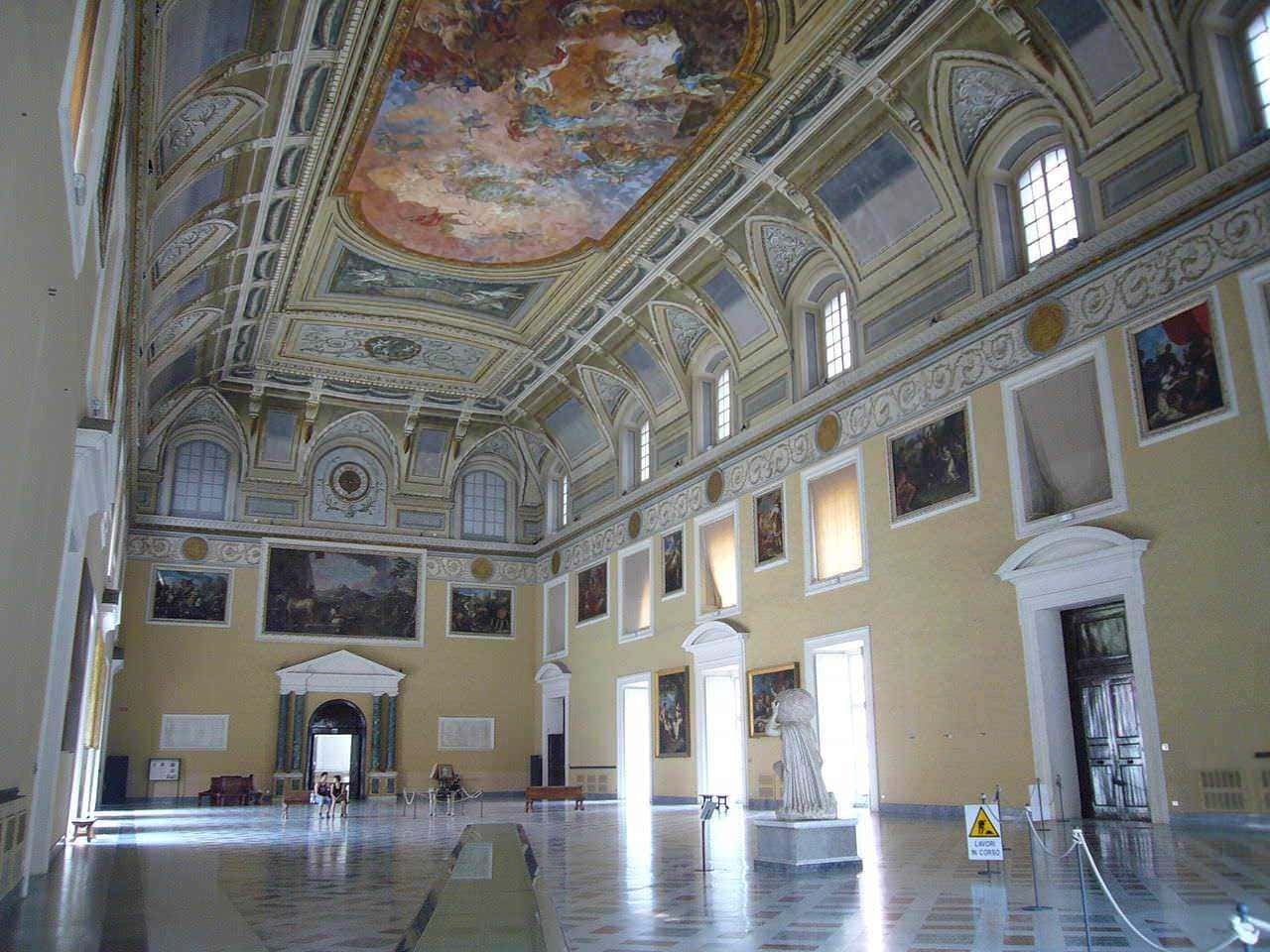 Museo storico con soffitto dipinto e pareti riccamente decorate, illuminato da grandi finestre, con statue e opere d'arte classiche, ambiente elegante e affascinante.