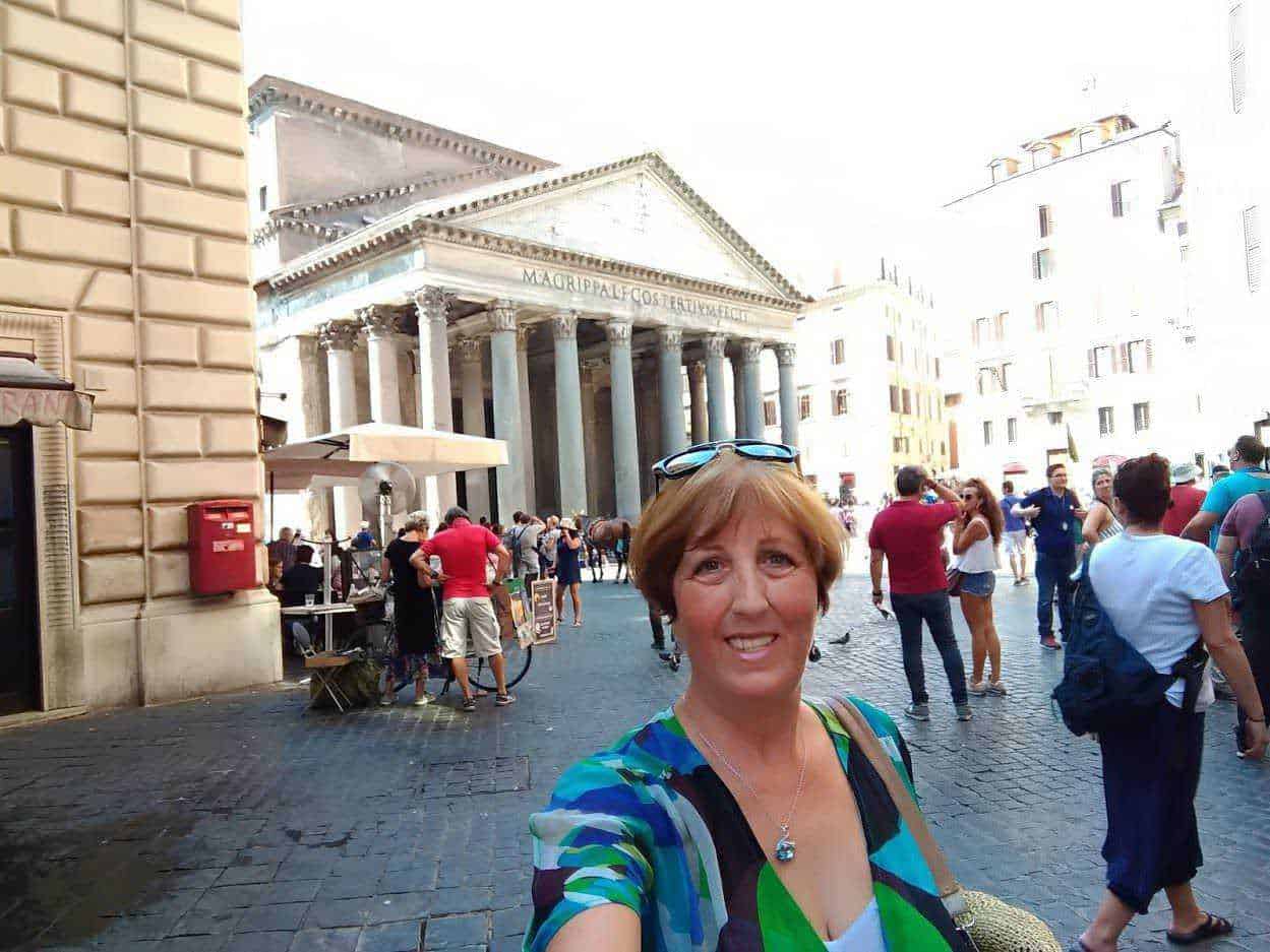 Antica piazza romana con il Pantheon sullo sfondo, turista sorridente che scatta selfie a Roma, edificio storico e atmosfera vivace turistica.