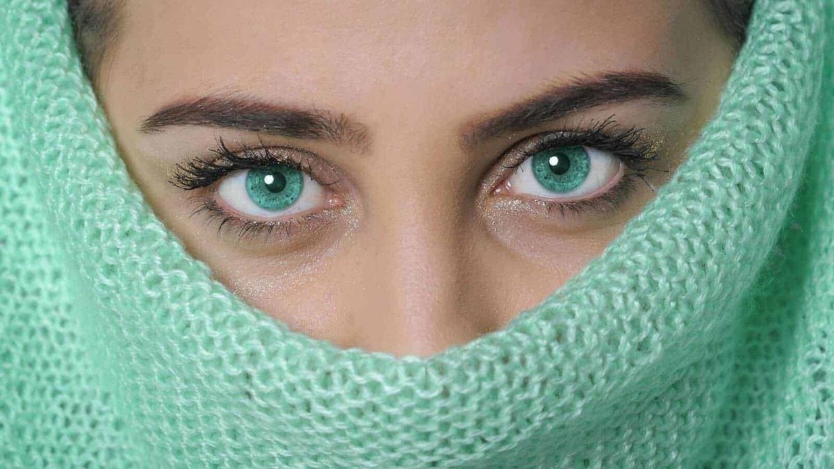 Occhi azzurri intensi di donna nascosta sotto sciarpa verde in tessuto a rete, primo piano, bellezza e stile.