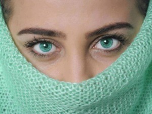 Occhi azzurri intensi di donna nascosta sotto sciarpa verde in tessuto a rete, primo piano, bellezza e stile.