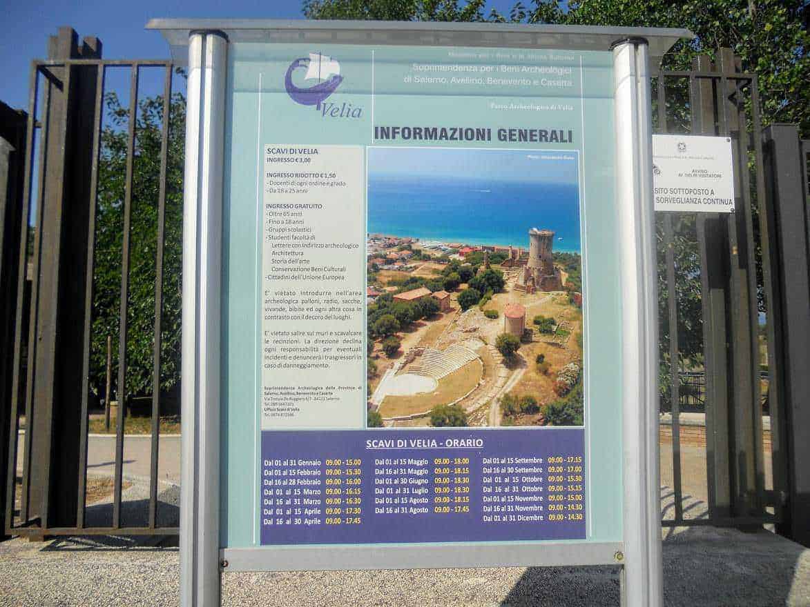 Costiera cilentana posti da visitare tra mare e terra 17 Pannello informativo esterno con panoramica archeologica di Velia, indicando orari di apertura e principali attrazioni, immerso in un ambiente naturale.