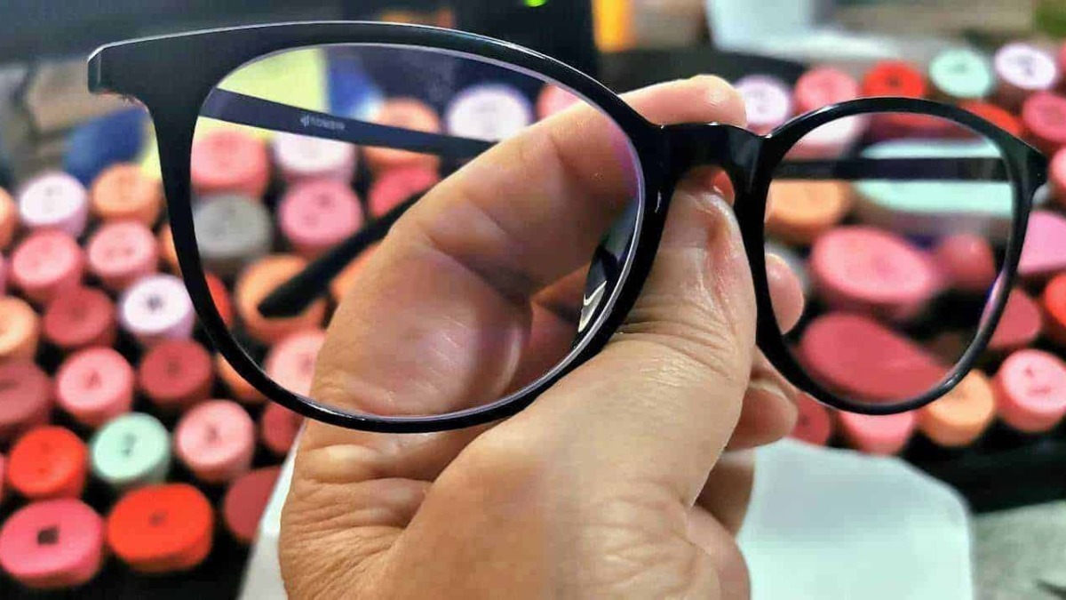 Occhiali da vista neri con montatura in plastica, in mano, contro sfondo di evidenziatori colorati, da usare come esempio di accessori moda e strumenti di correzione visiva.