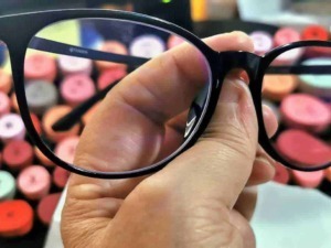 Occhiali da vista neri con montatura in plastica, in mano, contro sfondo di evidenziatori colorati, da usare come esempio di accessori moda e strumenti di correzione visiva.