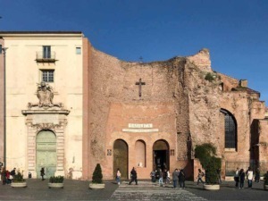 Antica chiesa e rovine storiche di Roma, ingresso alla basilica con archi e croce, scena urbana con persone, cielo blu e elementi di architettura religiosa, centro storico, monumento storico.