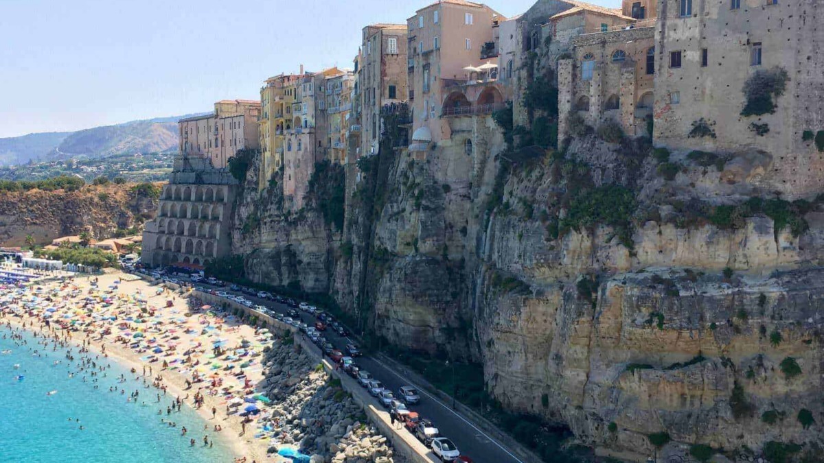 Ville sulla scogliera a Positano con spiaggia affollata e acque cristalline, vista panoramica delle case colorate e delle strade costiere, meta turistica famosa sulla Costiera Amalfitana, Italia.