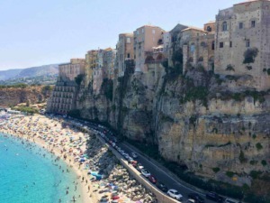 Ville sulla scogliera a Positano con spiaggia affollata e acque cristalline, vista panoramica delle case colorate e delle strade costiere, meta turistica famosa sulla Costiera Amalfitana, Italia.
