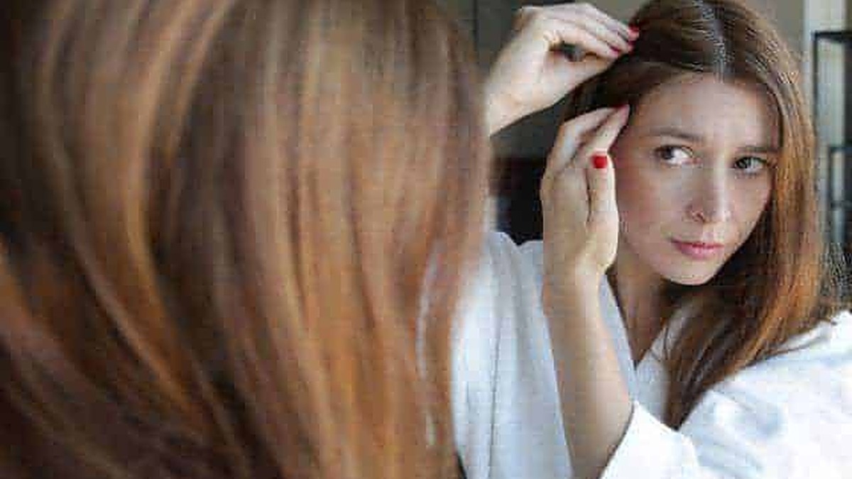 Capelli rossi, donna che si sistema i capelli di fronte allo specchio, cura della bellezza, hair care, routine di bellezza, look personalizzato, autostima, stile e immagine.