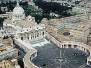 Immagine aerea di San Pietro e Piazza San Pietro a Roma, con la basilica e le statue storiche, vista dall'alto durante il giorno.