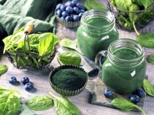 Succo di spirulina verde in barattoli di vetro con foglie di spinaci e bacche di mirtillo, ambiente naturale.