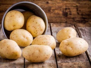 Patate novelle fresche disposte su un tavolo di legno rustico, con alcune spillate da un secchio di metallo, perfette per ricette di cucina casalinga e dietetiche.