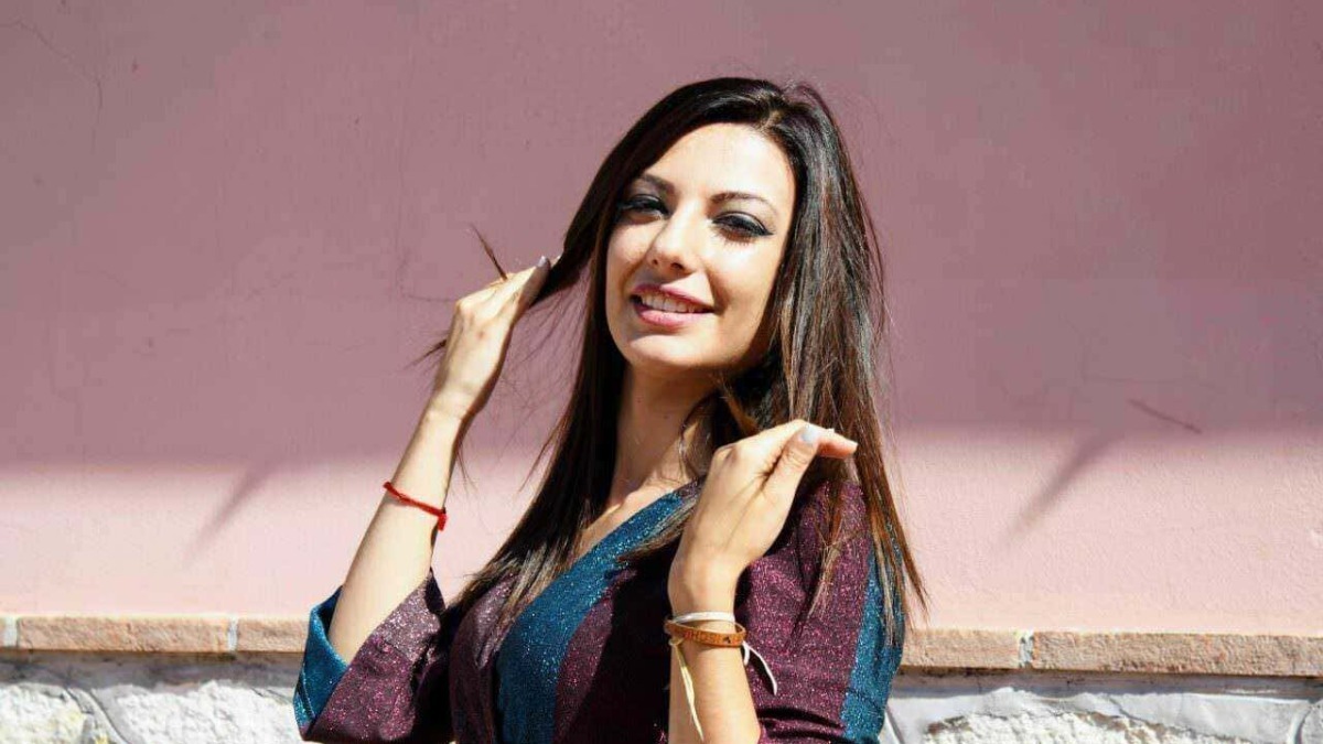 Bellissima donna con capelli lunghi e trucco elegante, posa in esterno vicino a una parete rosa, stile casual chic. Perfetta immagine per blog di moda, lifestyle e tendenze femminili.