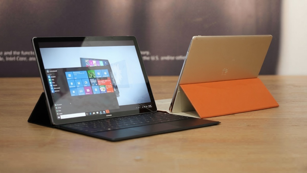 Laptop Microsoft Surface con tastiera e tablet con cover in bianco e arancione su scrivania di legno, tecnologia moderna.
