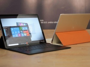 Laptop Microsoft Surface con tastiera e tablet con cover in bianco e arancione su scrivania di legno, tecnologia moderna.